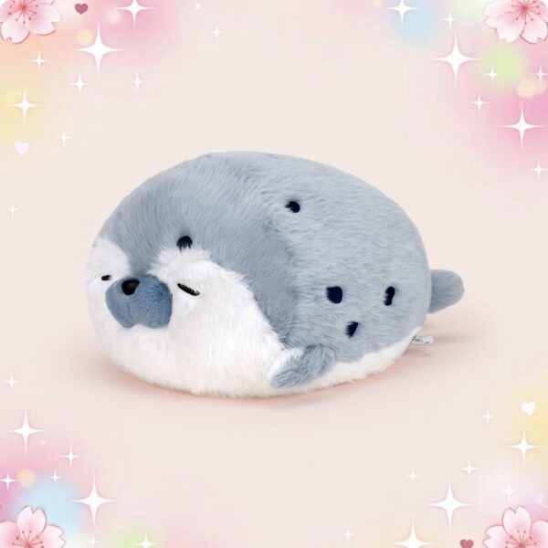 Un doudou kawaii otarie ronde tout doux et gris, en forme de petite otarie moelleuse avec un visage blanc, posé sur un fond rose pastel décoré d’étoiles et de fleurs.