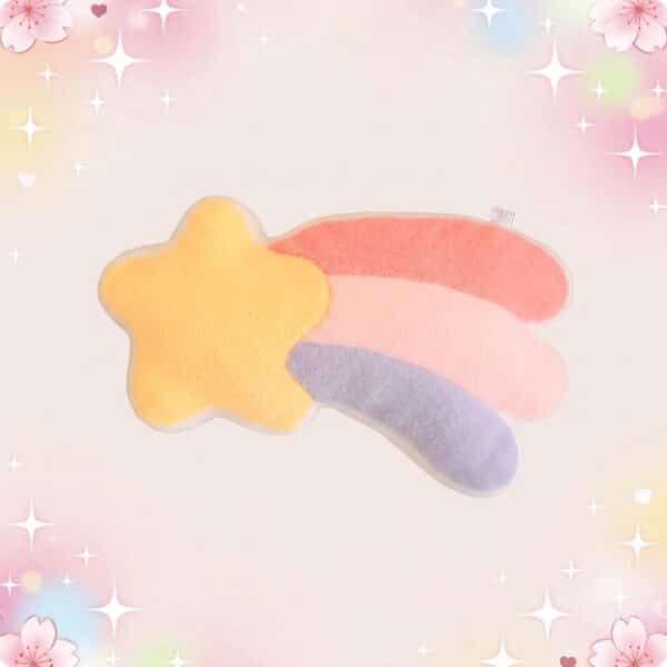 Un coussin kawaii étoile filante en forme de grosse étoile jaune avec une queue arc-en-ciel rose, bleu et violet, posé sur un fond pastel décoré d’étoiles et de fleurs.