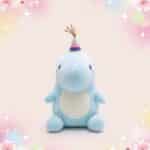 Une peluche dinosaure kawaii d'anniversaire bleu clair avec un chapeau de fête rayé, assise sur un fond rose pastel avec des étoiles et des fleurs scintillantes.