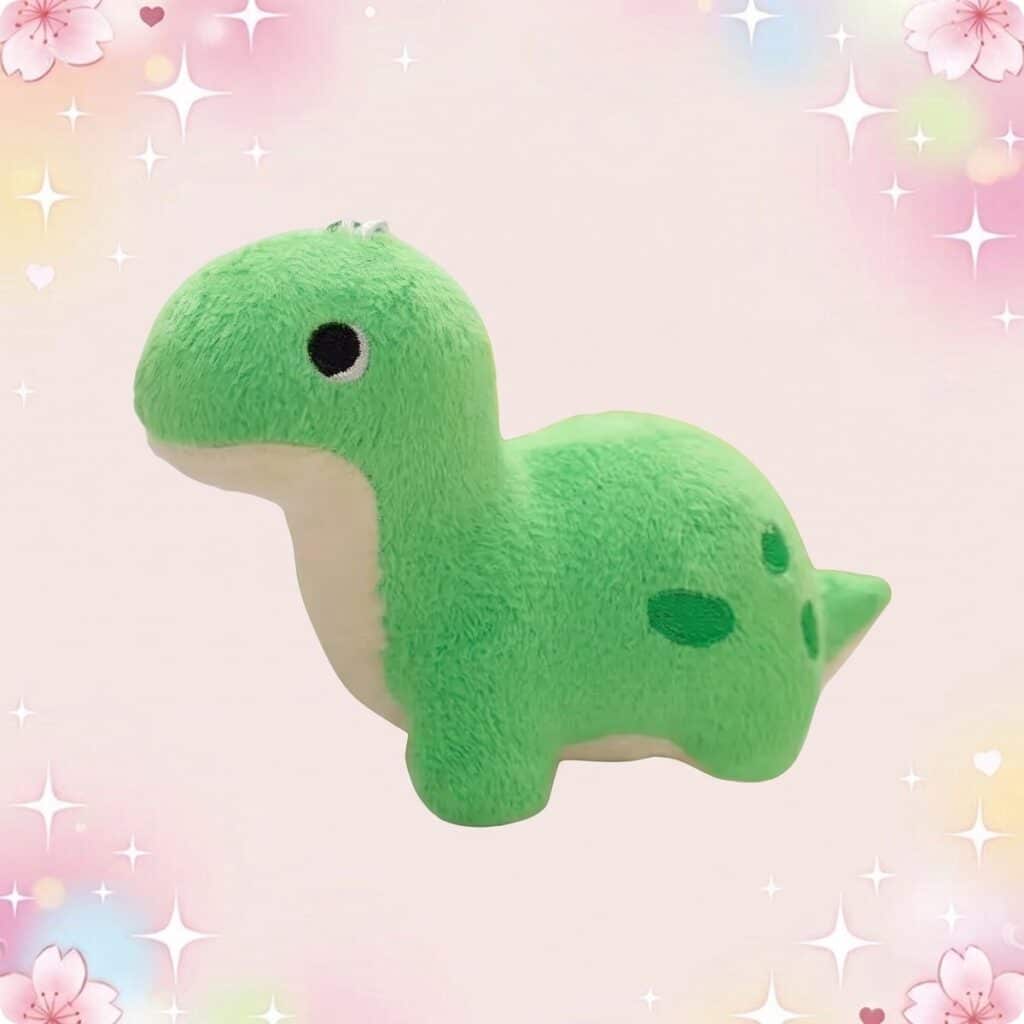 Une peluche petit dinosaure kawaii coloré verte, douce et ronde, avec un petit visage mignon, sur un fond rose pastel avec des étoiles et des cœurs.