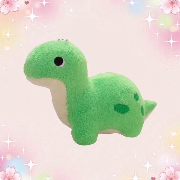Une peluche petit dinosaure kawaii coloré verte, douce et ronde, avec un petit visage mignon, sur un fond rose pastel avec des étoiles et des cœurs.