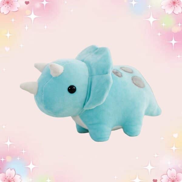 Une peluche dinosaure kawaii pastel bleue, douce et ronde, avec petites cornes blanches, posée sur un fond rose décoré d’étoiles et de fleurs.