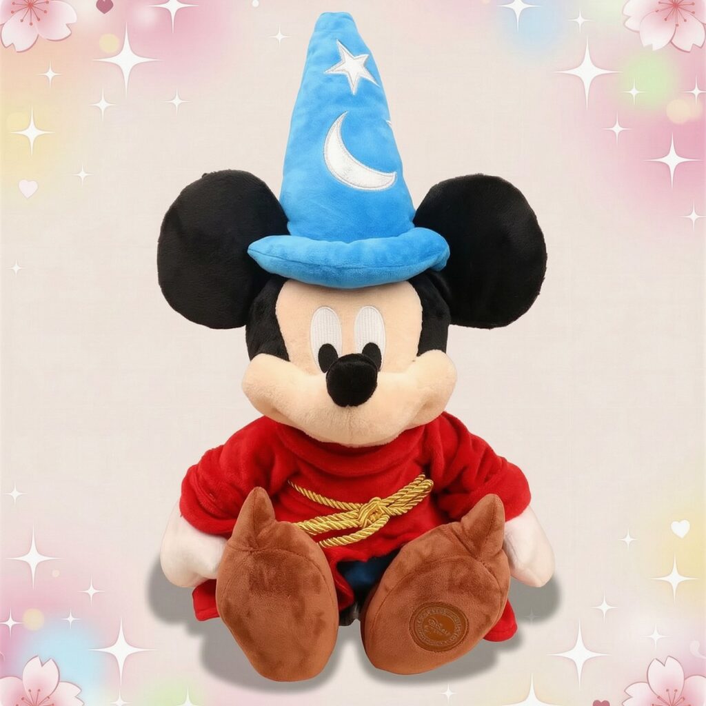 Une peluche Mickey déguisé en magicien avec un grand chapeau bleu, une robe rouge et des chaussures marron, posée sur un fond clair décoré d’étoiles et de cœurs.