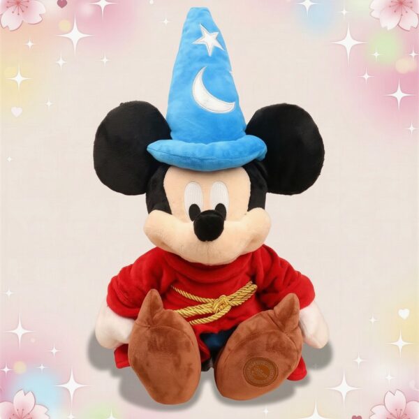 Une peluche Mickey déguisé en magicien avec un grand chapeau bleu, une robe rouge et des chaussures marron, posée sur un fond clair décoré d’étoiles et de cœurs.