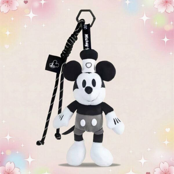 Une peluche Mickey format porte-clés en noir et blanc, suspendue à un cordon, sur un fond doux avec des étoiles et des cœurs.