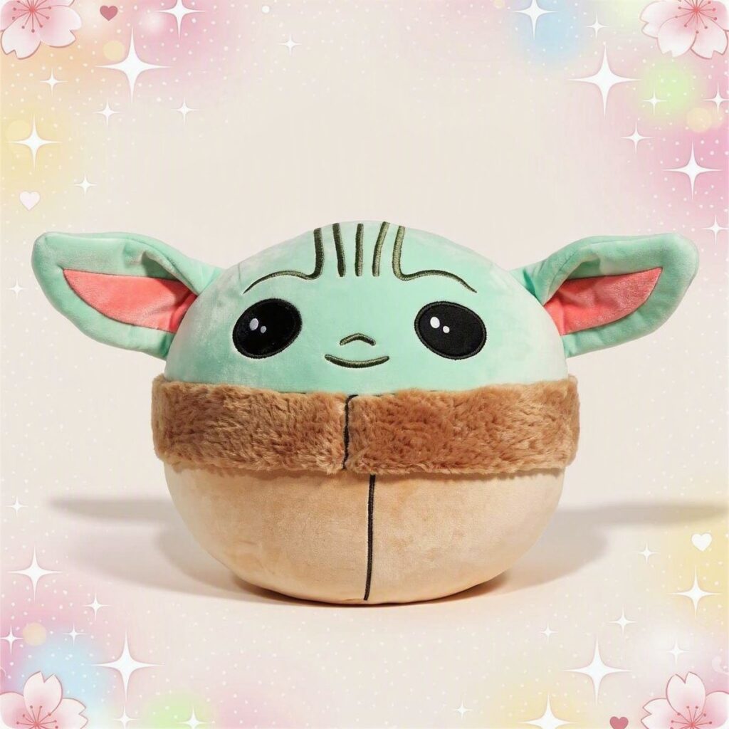 Une peluche Squishmallow bébé Yoda toute ronde et douce, avec de grandes oreilles vertes, de grands yeux noirs et un petit manteau brun, sur un fond pastel avec des étoiles et des cœurs.