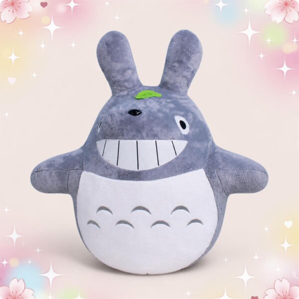 Une Peluche Totoro souriant grise et moelleuse, avec de grandes oreilles, un grand sourire blanc et un ventre rond, posée sur un fond pastel avec des étoiles et des cœurs.