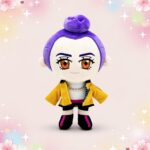 Une peluche Kpop Demon Hunters Rumi violette avec grand visage, yeux orange, veste jaune et petites bottes, posée sur un fond rose pastel avec des étoiles.
