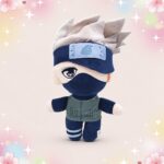 Une peluche Naruto Kakashi au masque et cheveux argentés, debout sur un fond pastel décoré de petites étoiles et de fleurs.