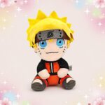 Une peluche Naruto Uzumaki position assise, avec cheveux jaunes, grand bandeau et tenue orange et noire, assise au centre sur un fond rose décoré de petites étoiles et fleurs.