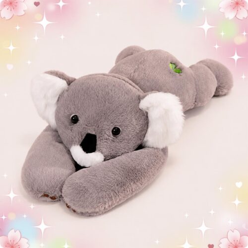 Une peluche koala grise aux bras longs et yeux noirs, allongée sur le ventre avec de grandes oreilles blanches, sur un fond doux et coloré.