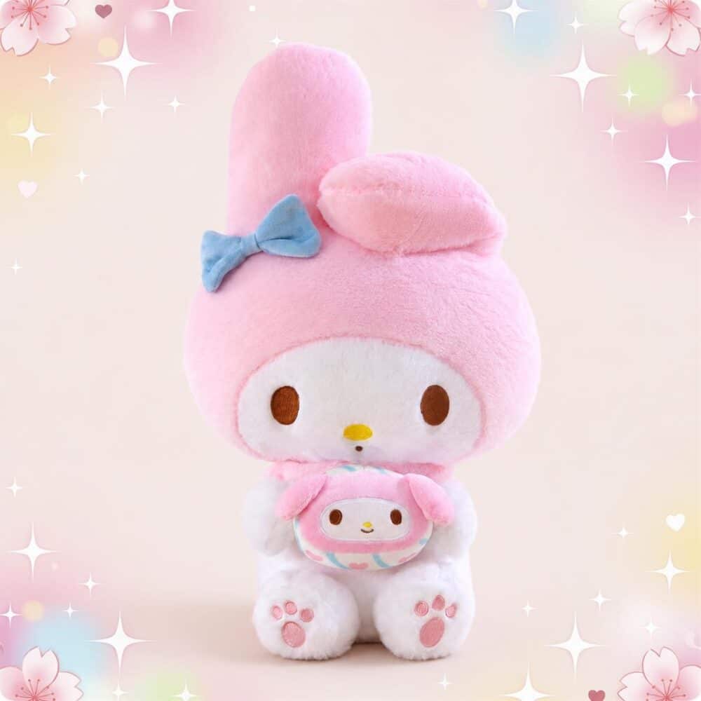 Une peluche My Melody rose et blanche grand format, avec un grand nœud bleu sur la tête et un petit doudou dans les bras, sur un fond rose tout doux avec des étoiles.