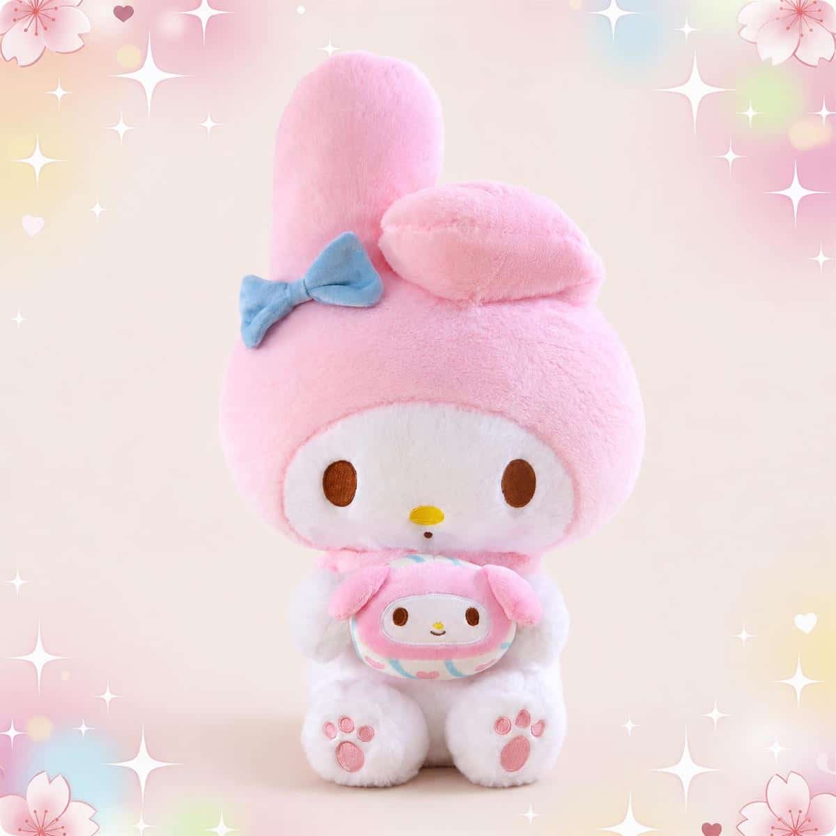 Une peluche My Melody rose et blanche grand format, avec un grand nœud bleu sur la tête et un petit doudou dans les bras, sur un fond rose tout doux avec des étoiles.