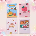 Quatre cahiers kawaii A5 à motif fruit, avec des dessins mignons de fruits comme une fraise, un ananas et une orange, posés sur un fond rose tendre.