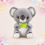 Une peluche Koala gris avec feuille verte au cou, assise toute douce avec de grands yeux, sur un fond pastel avec des étoiles et des fleurs.