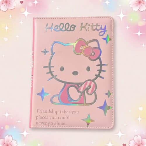 Un carnet de note Hello Kity à couverture en simili cuir rose, avec un grand dessin de Hello Kitty et des étoiles brillantes, posé sur un fond doux et pastel.