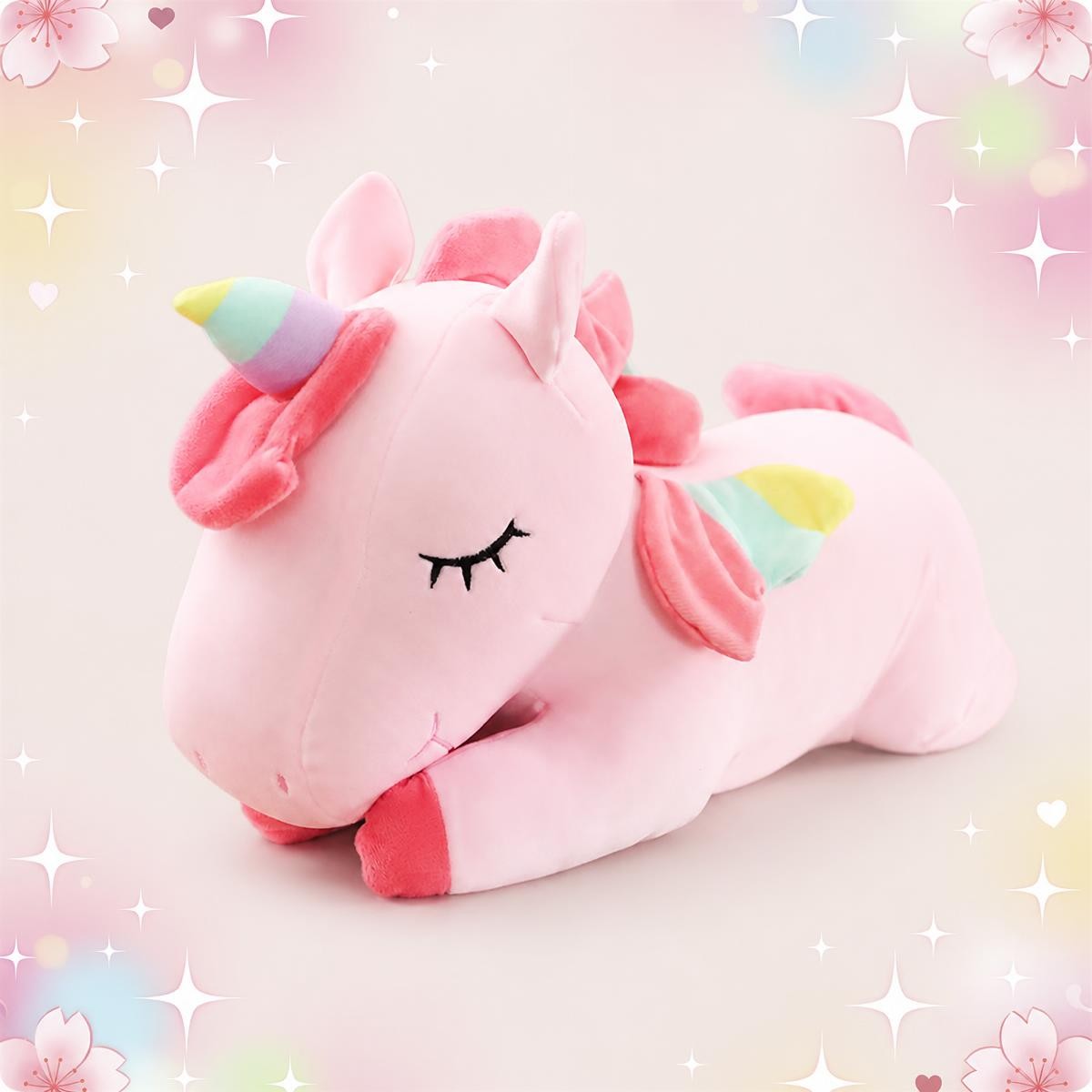 Une peluche licorne endormie grand format rose, avec une corne arc-en-ciel et des yeux fermés, posée sur un fond doux et décoré d’étoiles.