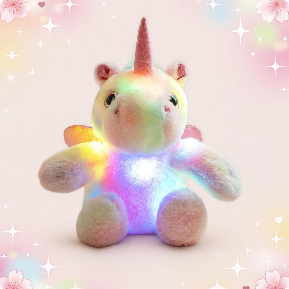 Une peluche licorne lumineuse en tissu doux, assise et brillant de couleurs arc-en-ciel, avec une corne rose et un fond rose décoré d’étoiles et de petits cœurs.