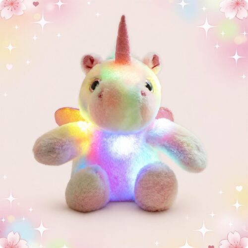 Une peluche licorne lumineuse en tissu doux, assise et brillant de couleurs arc-en-ciel, avec une corne rose et un fond rose décoré d’étoiles et de petits cœurs.