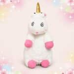 Une peluche licorne Moi Moche et Méchant blanche avec corne dorée, yeux en spirale et pattes roses, posée sur un fond rose décoré d’étoiles brillantes.
