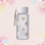 Une gourde kawaii transparente à motif marguerite grise avec un cordon, posée sur un fond rose pastel décoré de petites étoiles et fleurs.