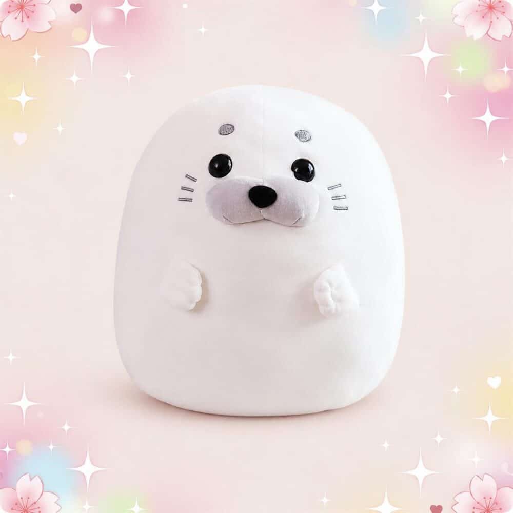 Une peluche animal kawaii phoque squishymallow blanche et toute ronde, avec de grands yeux noirs et un petit museau, posée sur un fond rose pastel avec des étoiles et des fleurs.