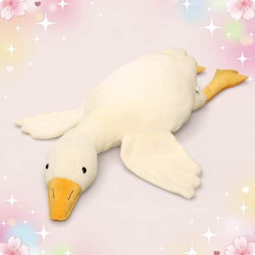 Une peluche canard géante blanche, allongée sur un fond rose décoré de petites étoiles et de fleurs, avec un grand bec jaune et des ailes douces.