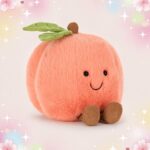Une peluche Jellycat Amuseables Peach en forme de pêche rose toute douce, avec de petites feuilles vertes, un sourire brodé et de petits pieds marron, posée sur un fond pastel avec des étoiles.
