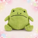 Une peluche Jellycat Ricky Rain Frog verte, toute ronde et douce, avec de petits yeux noirs et une bouche sérieuse, posée sur un fond pastel décoré d’étoiles et de fleurs.