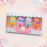 Une boîte de Gomme Kawaii imitant une sucette bien ronde lot de 3 boites, avec quatre gommes colorées en forme de sucette à ruban, sur un fond rose décoré d’étoiles.