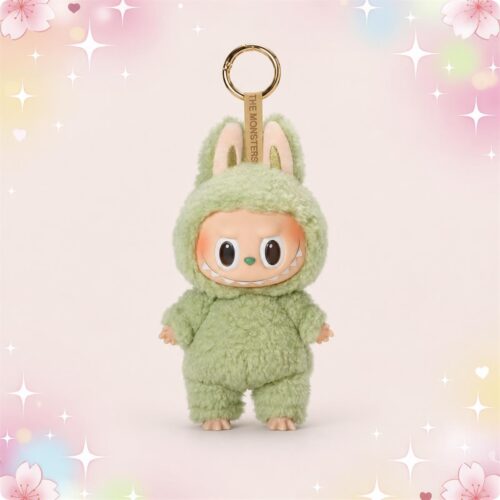 Un porte-clé peluche Labubu vert tout doux, avec de grandes oreilles et un anneau doré, posé sur un fond rose pastel avec des étoiles brillantes.