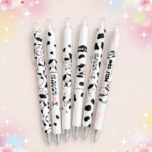 Plusieurs stylo Kawaii vache à pointe extra fine posés sur un fond rose décoré d’étoiles, avec des motifs de vaches noires et blanches mignonnes.