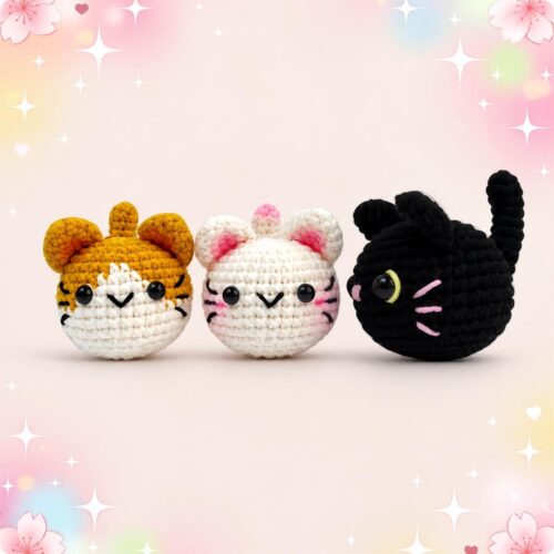 Trois peluches crochetées en forme de chats, avec le kit amigurumi trois chats kawaii, posées sur un fond rose pastel décoré d’étoiles et de fleurs.