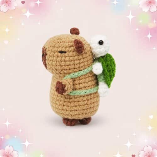 Un petit capibara en crochet portant une tortue sur son dos, avec une carapace verte et un fond pastel décoré d’étoiles et de fleurs.