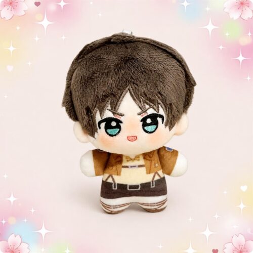 Une mini peluche anime Eren de l'Attaque des Titans, avec de grands yeux et un uniforme marron, sur un fond rose décoré de petites étoiles.