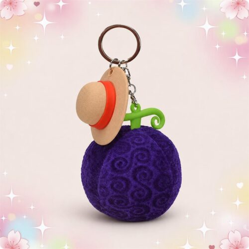 Une mini peluche fruit du démon de Luffy format porte-clés violette, avec un chapeau de paille au-dessus, posée sur un fond pastel décoré d’étoiles et de fleurs.