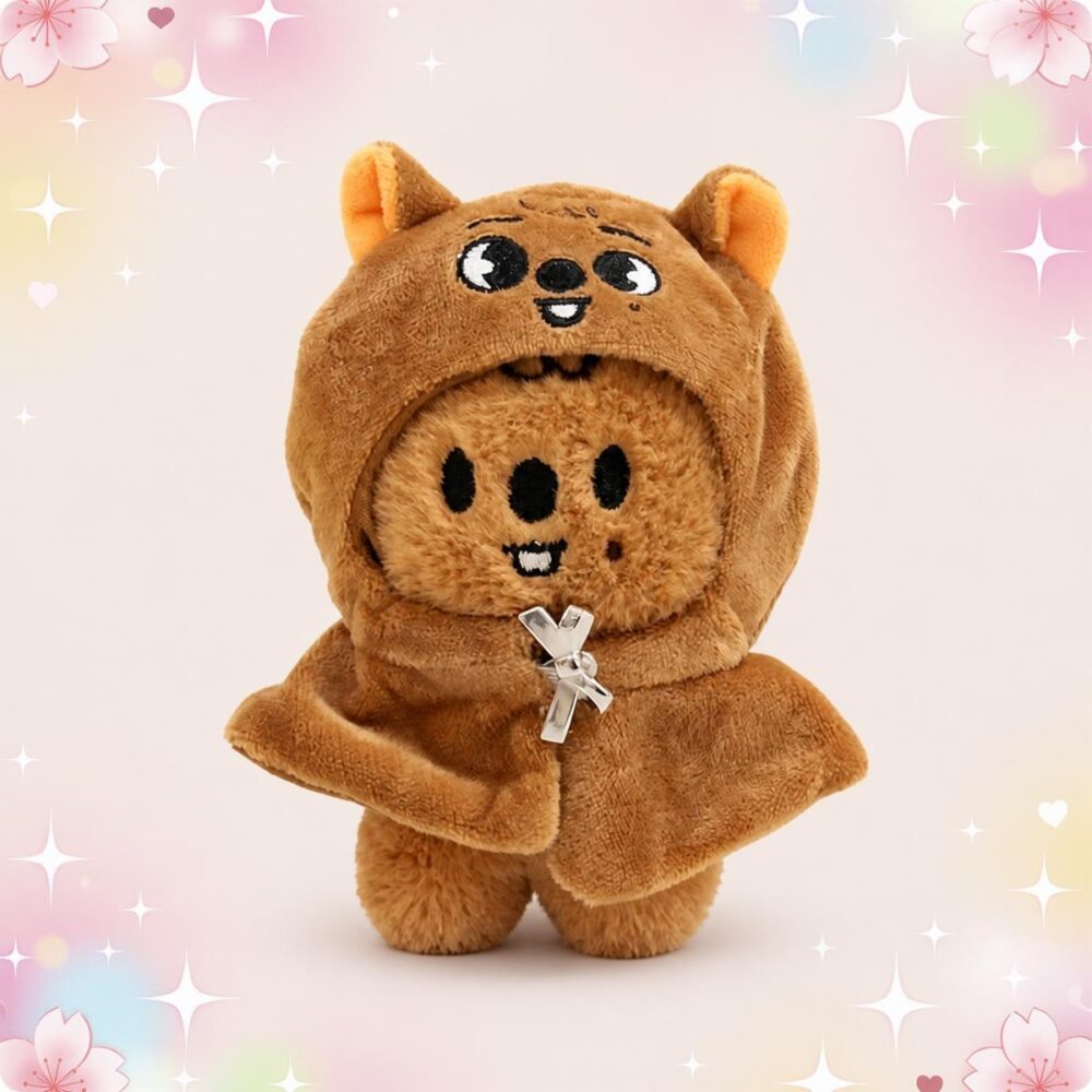 Une mini peluche SKZOO Han Quokka brune en forme de petit animal, avec une capuche à oreilles et un petit sourire, sur fond pastel décoré d’étoiles et de fleurs.