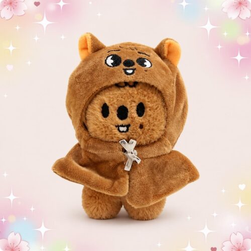 Une mini peluche SKZOO Han Quokka brune en forme de petit animal, avec une capuche à oreilles et un petit sourire, sur fond pastel décoré d’étoiles et de fleurs.