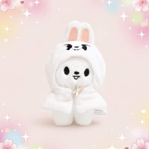 Une mini peluche SKZOO Leebit blanche en costume de lapin, avec de grandes oreilles et un petit sourire, sur un fond rose doux et scintillant.