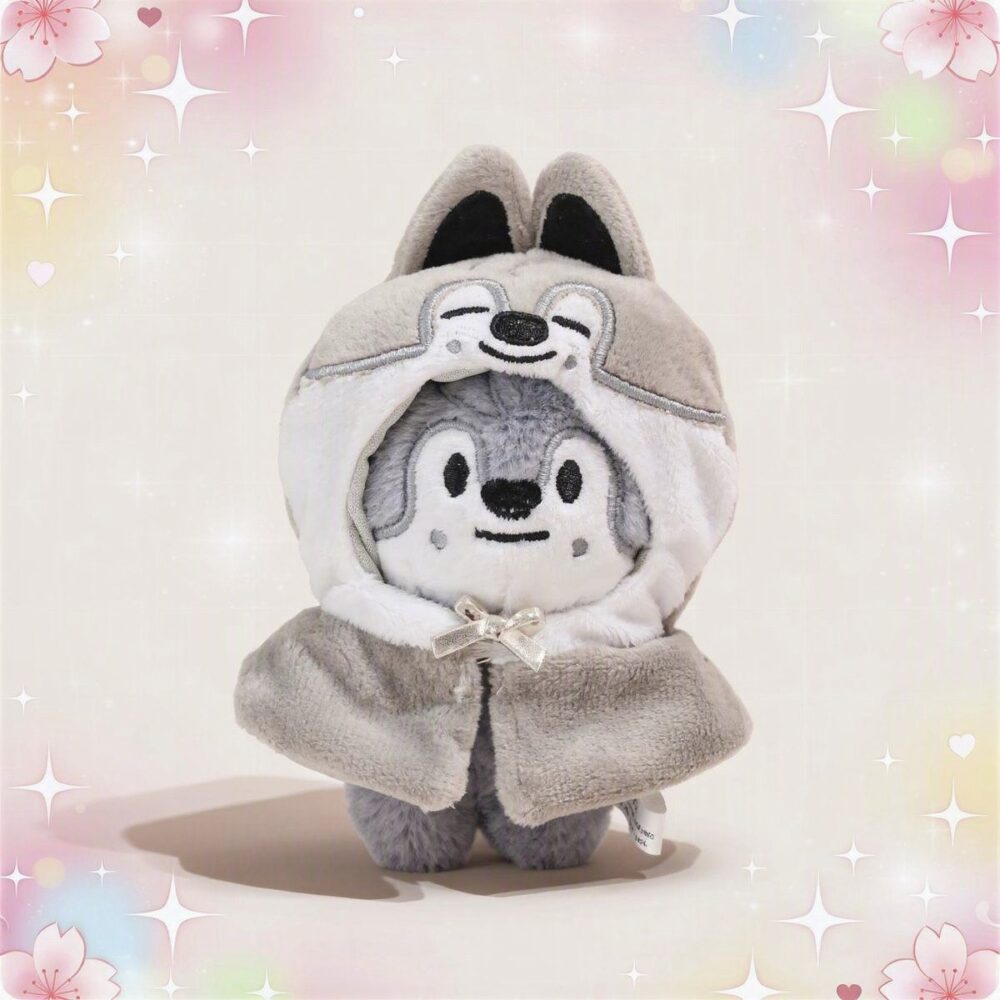 Une mini peluche SKZOO Wolf Chan grise et blanche, avec une capuche à oreilles de loup et un petit ruban, posée sur un fond doux et brillant.