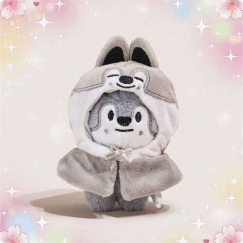 Une mini peluche SKZOO Wolf Chan grise et blanche, avec une capuche à oreilles de loup et un petit ruban, posée sur un fond doux et brillant.