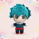 Une peluche anime Izuku Midoriya version porte-clés, représentant un petit personnage aux cheveux bleus et à l’uniforme vert, sur un fond rose décoré de cœurs et d’étoiles.