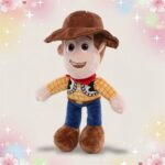 Une peluche Disney Woody de Toy Story debout, avec un grand chapeau brun, une chemise jaune, un foulard rouge, un pantalon bleu et de grosses bottes, sur un fond pastel avec des étoiles et des cœurs.