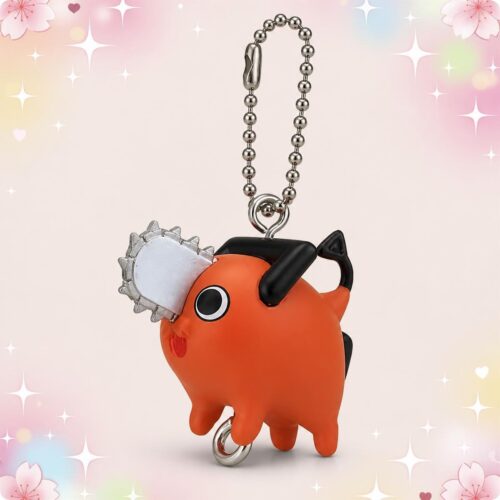 Une Figurine Gachapon Pochita de Chainsaw Man orange en forme de petit chien, avec une mini tronçonneuse, suspendue à une chaîne boule sur fond rose décoré d’étoiles.