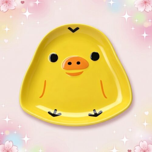 Une assiette de la vaisselle kawaii en céramique design poussin, jaune et en forme de petit poussin souriant, sur un fond rose décoré d’étoiles et de fleurs.
