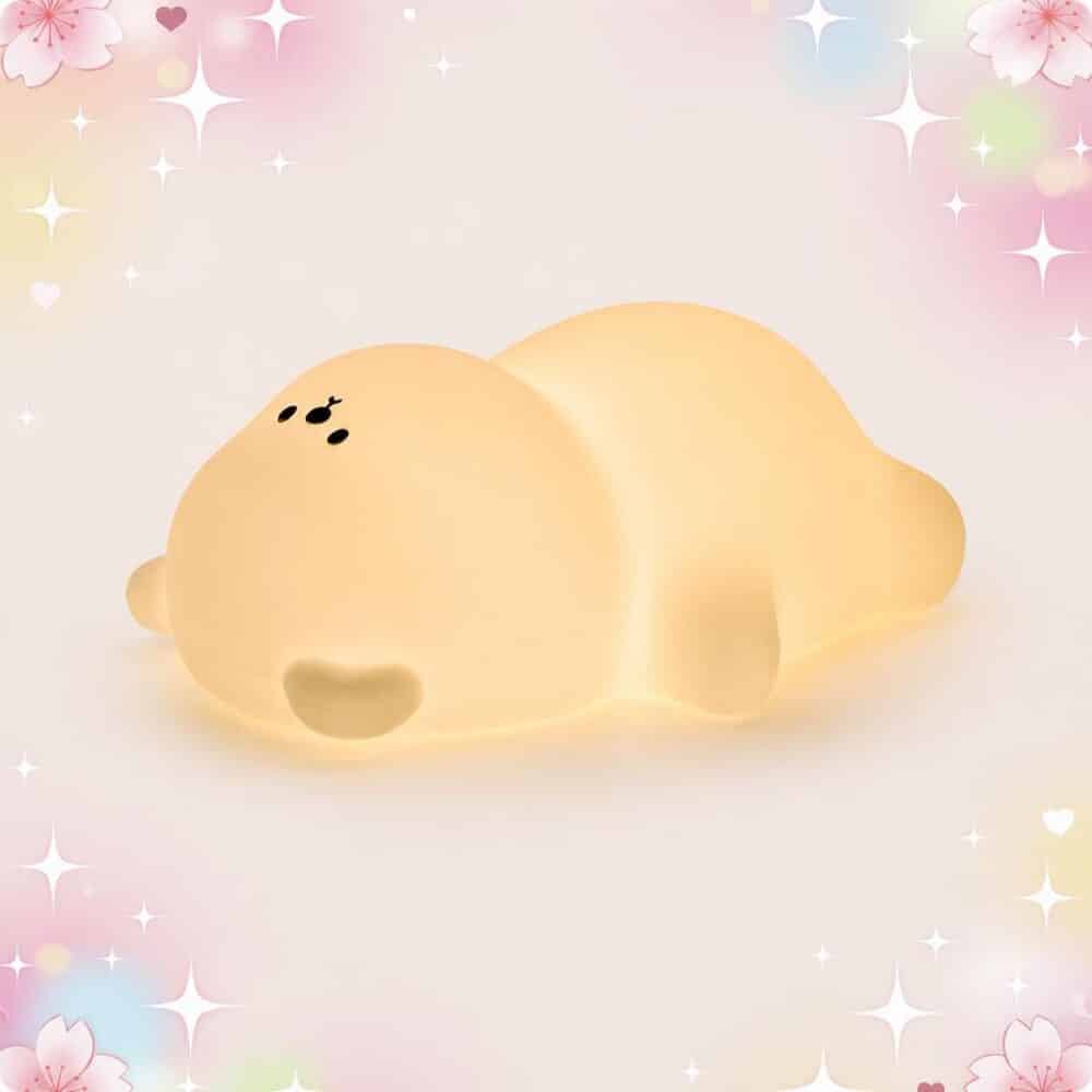 Une douce Veilleuse Kawaii en ourson allongé sur le ventre, en forme de petit ours jaune qui brille, sur un fond pastel avec des étoiles et des cœurs.