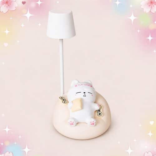 Une lampe kawaii chat de bureau au thème gamer avec un petit chat blanc allongé sur un coussin beige, sous un abat-jour blanc, sur fond rose pastel décoré d’étoiles.