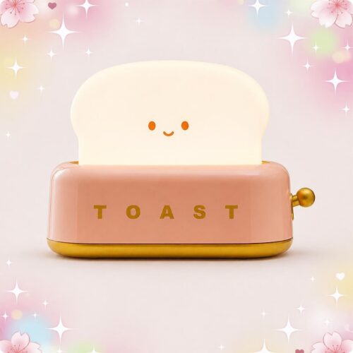 Une petite veilleuse en forme de grille pain souriante, avec une tranche de pain lumineuse au-dessus et un fond rose décoré d’étoiles et de cœurs.