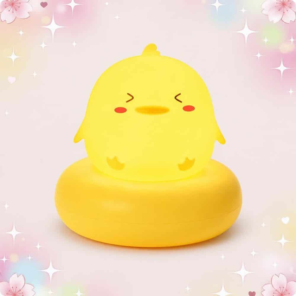 Une Veilleuse Kawaii en canard aux allures de dessin animé jaune, posée sur une base ronde, avec un fond rose pastel rempli de petites étoiles et de cœurs.
