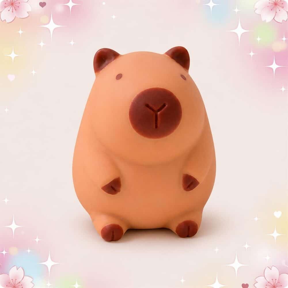 Un Anti-stress squishy Capybara en forme de petit capybara brun à presser, posé sur un fond pastel avec des étoiles et des fleurs.